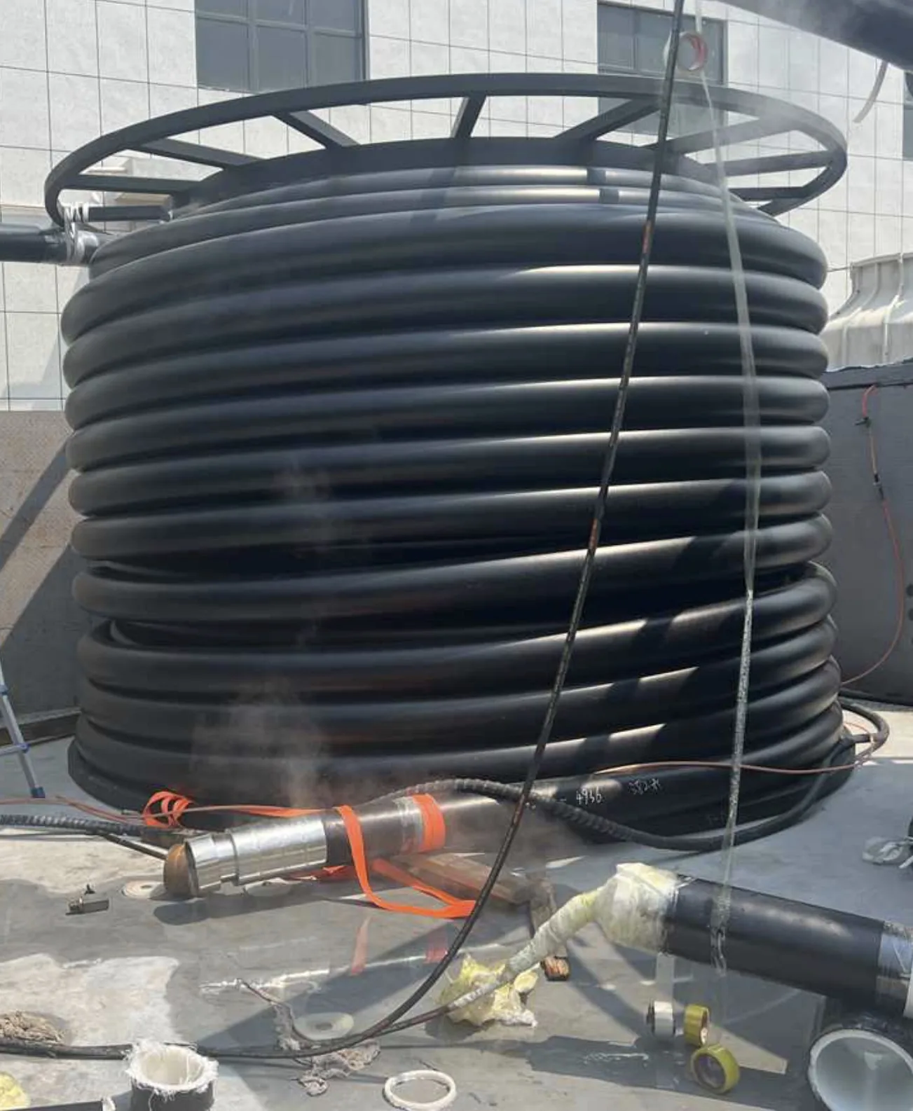 Black composite line pipe on a metal reel in an industrial yard